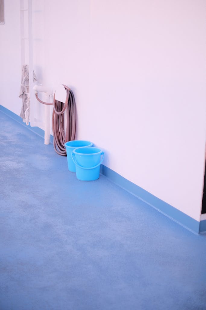 A minimalist composition of two blue buckets against a white wall with a hose nearby.