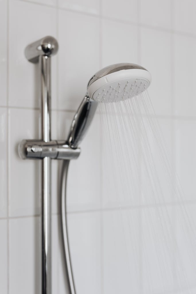 Close-up of a chrome shower head with water flowing, showcasing sleek modern bathroom design.