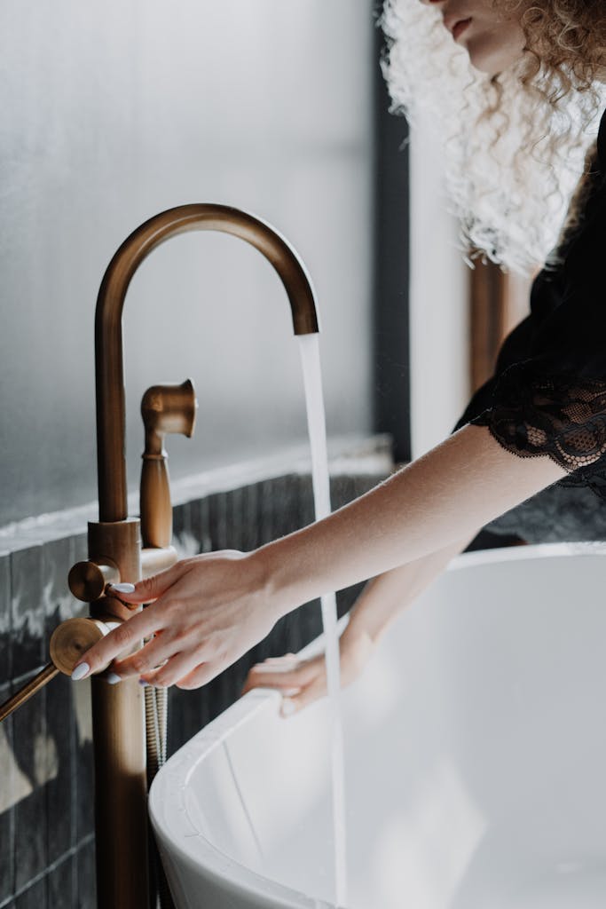 Elegant bathroom scene with a focus on gold faucet and female hands adjusting water flow.