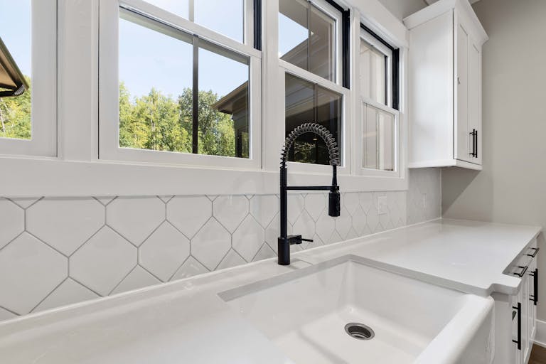 White kitchen countertop with black faucet, large windows, and modern cabinetry