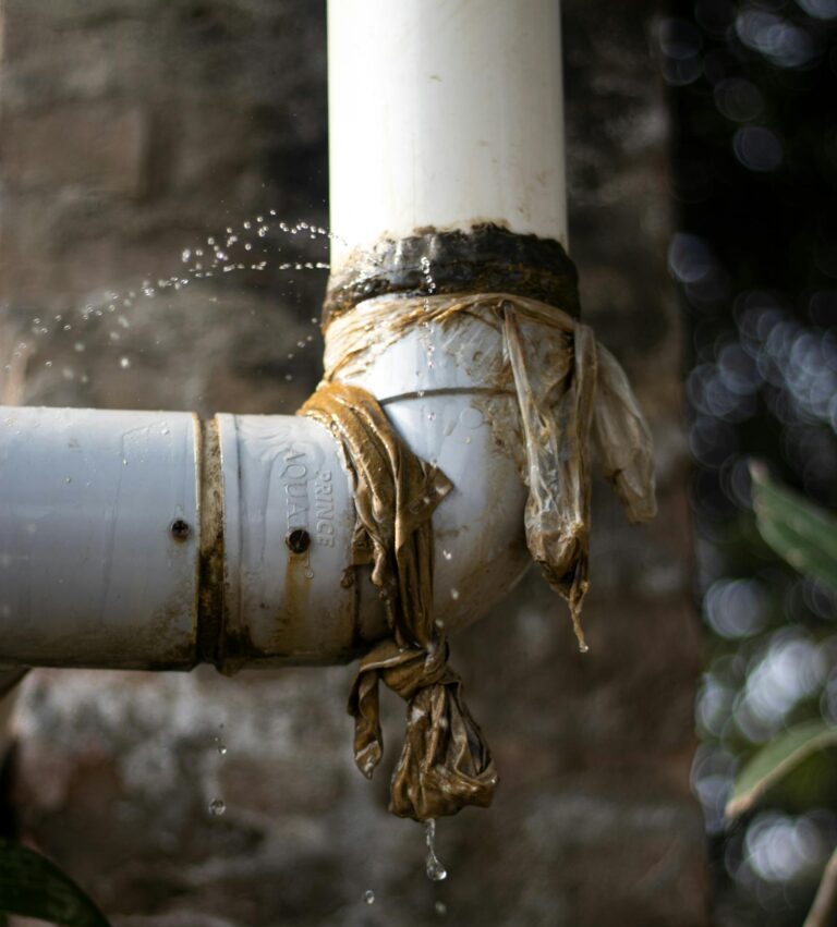 Close-up of a leaking plastic pipe outdoors with water dripping, showing wear and tear.